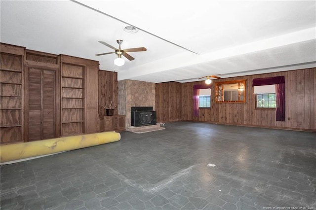 unfurnished living room with ceiling fan, a wood stove, and wooden walls