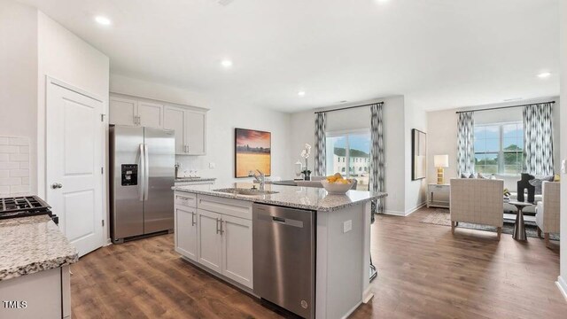 kitchen with light stone countertops, appliances with stainless steel finishes, dark hardwood / wood-style flooring, a kitchen island with sink, and sink