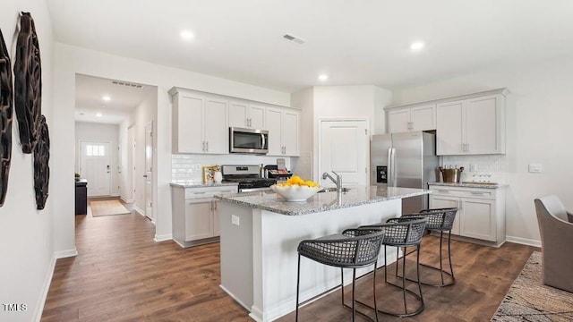 kitchen with a kitchen bar, appliances with stainless steel finishes, light stone counters, a center island with sink, and dark hardwood / wood-style floors