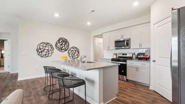 kitchen with light stone counters, a breakfast bar, stainless steel appliances, a center island with sink, and dark hardwood / wood-style floors