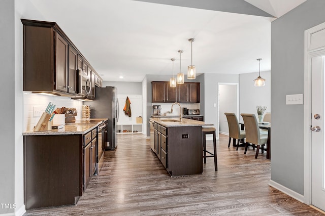 kitchen featuring appliances with stainless steel finishes, dark brown cabinetry, a kitchen island with sink, and wood-type flooring