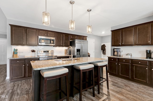 kitchen with a kitchen island with sink, sink, dark hardwood / wood-style floors, appliances with stainless steel finishes, and decorative light fixtures