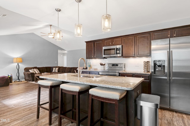 kitchen featuring sink, stainless steel appliances, lofted ceiling, decorative light fixtures, and a kitchen island with sink