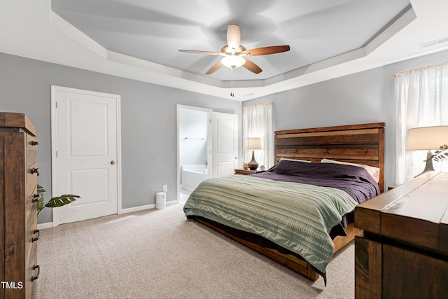 bedroom featuring a tray ceiling, ensuite bath, ceiling fan, and light carpet