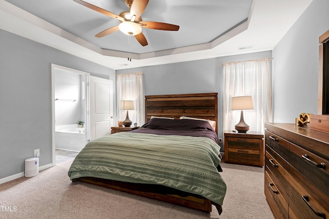 bedroom with ensuite bathroom, ceiling fan, a raised ceiling, and light carpet