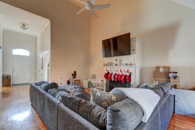 living room with hardwood / wood-style floors, a tile fireplace, a high ceiling, crown molding, and ceiling fan