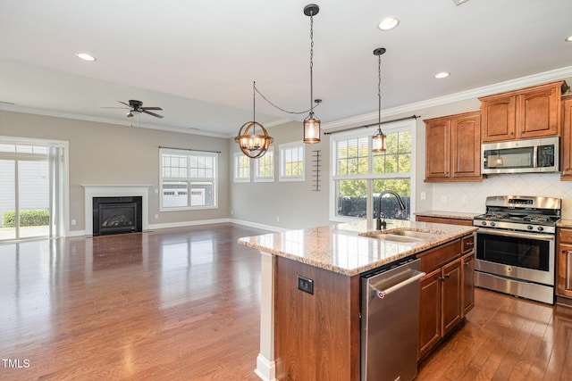 kitchen featuring sink, stainless steel appliances, light stone counters, decorative light fixtures, and a center island with sink