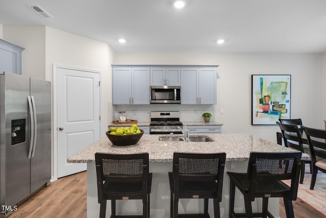 kitchen with a kitchen island with sink, sink, light hardwood / wood-style floors, light stone counters, and stainless steel appliances