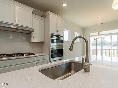 kitchen with white cabinetry, sink, light stone countertops, stainless steel appliances, and tasteful backsplash