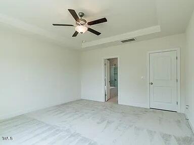 unfurnished bedroom featuring ceiling fan, visible vents, a tray ceiling, and ensuite bathroom