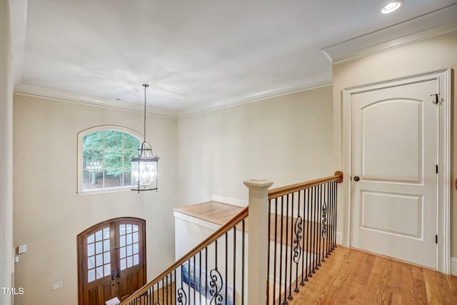 corridor featuring light wood-type flooring, french doors, ornamental molding, and a notable chandelier