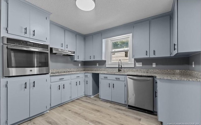 kitchen with gray cabinets, sink, light wood-type flooring, stainless steel appliances, and a textured ceiling