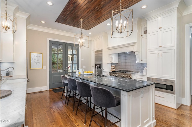 kitchen featuring stainless steel appliances, an island with sink, white cabinets, and dark stone counters