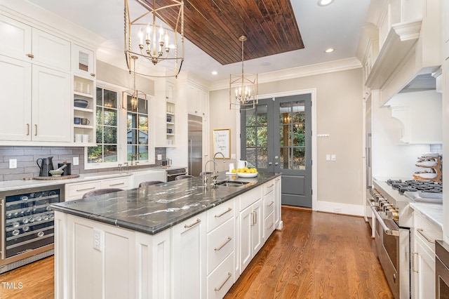 kitchen featuring high quality appliances, a center island with sink, sink, wine cooler, and white cabinetry