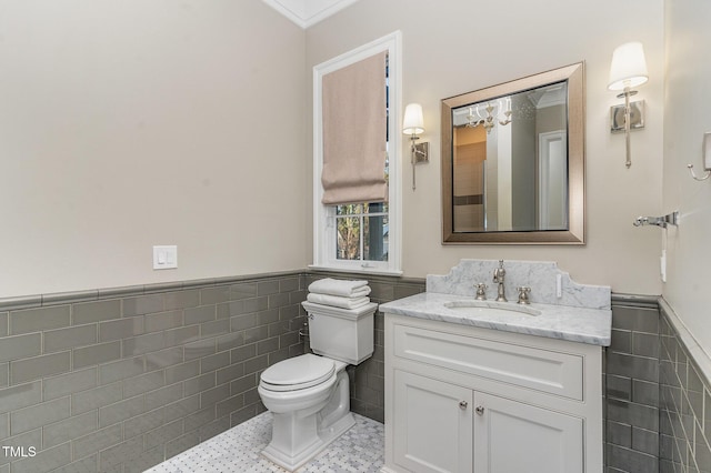 bathroom featuring tile patterned floors, crown molding, toilet, vanity, and tile walls