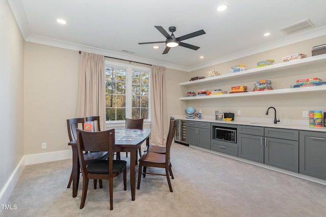 dining room with ceiling fan, sink, wine cooler, light colored carpet, and ornamental molding