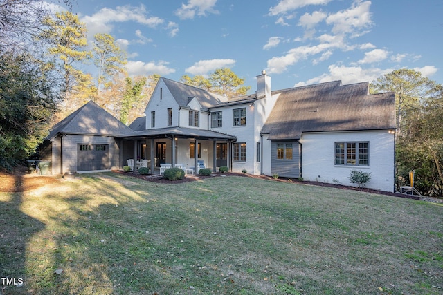 rear view of house with covered porch, a garage, and a lawn