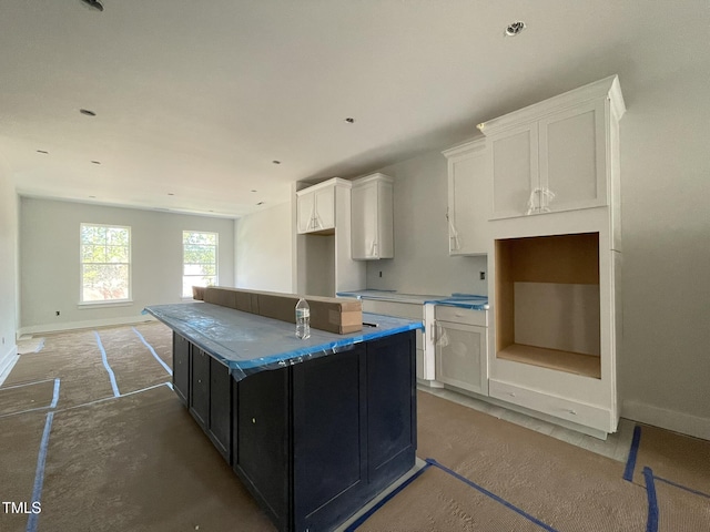 kitchen with dark cabinets, white cabinetry, a kitchen island, and baseboards