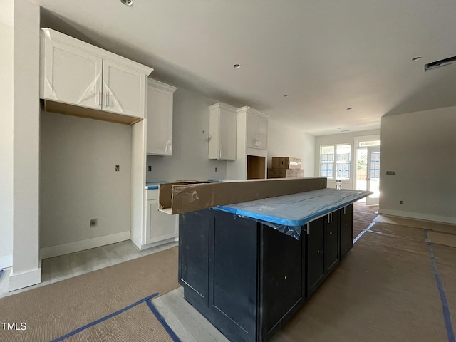 kitchen featuring baseboards, a kitchen island, white cabinetry, and dark cabinetry