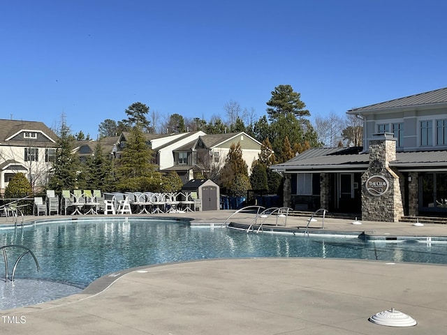 community pool featuring an outdoor structure, fence, a residential view, a shed, and a patio area