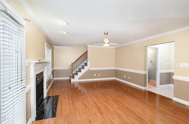 unfurnished living room featuring hardwood / wood-style flooring, ceiling fan, ornamental molding, and a premium fireplace