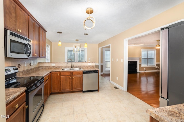 kitchen with light wood-type flooring, a textured ceiling, stainless steel appliances, sink, and decorative light fixtures