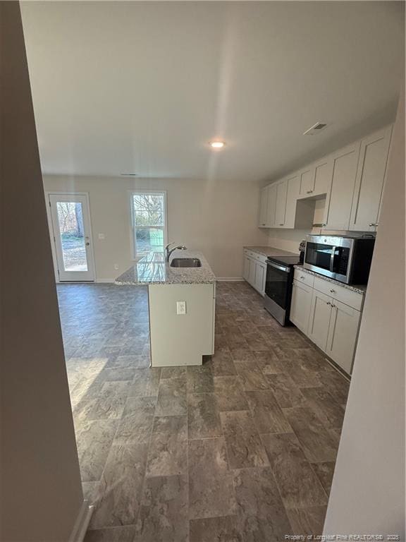 kitchen with a center island with sink, baseboards, white cabinets, appliances with stainless steel finishes, and a sink