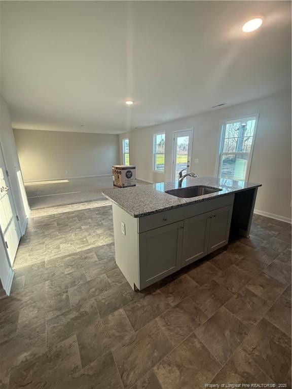 kitchen with a center island with sink, open floor plan, light stone countertops, a healthy amount of sunlight, and a sink