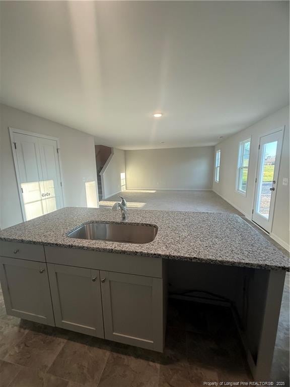 kitchen with a center island with sink, light stone counters, and a sink