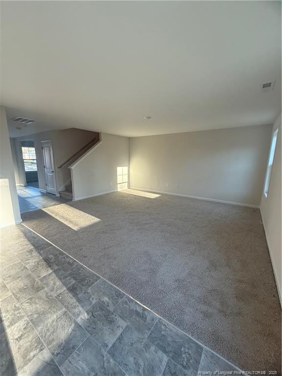 unfurnished living room featuring baseboards, stairs, visible vents, and carpet flooring