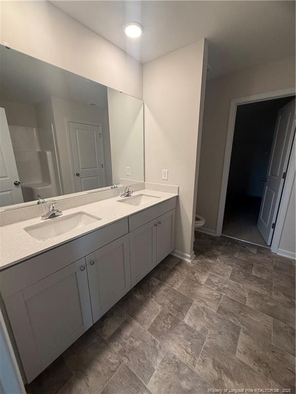 bathroom featuring toilet, double vanity, baseboards, and a sink