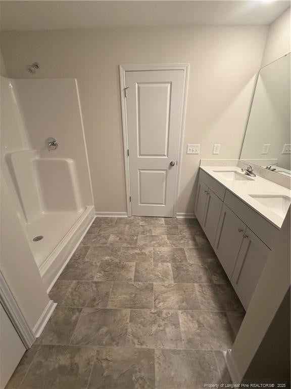 bathroom with a shower, double vanity, stone finish floor, a sink, and baseboards