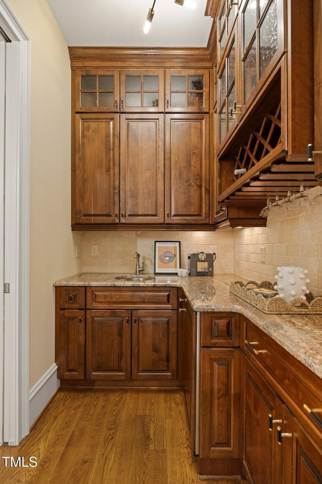 kitchen with hardwood / wood-style flooring, sink, backsplash, and light stone counters