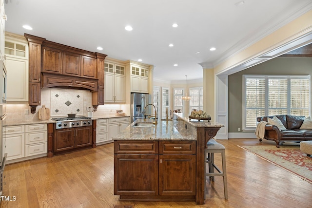 kitchen with sink, a breakfast bar area, light hardwood / wood-style flooring, appliances with stainless steel finishes, and an island with sink