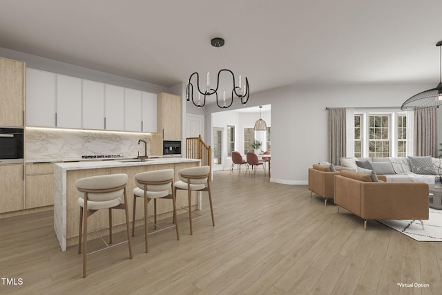 kitchen with light hardwood / wood-style flooring, hanging light fixtures, backsplash, an island with sink, and oven