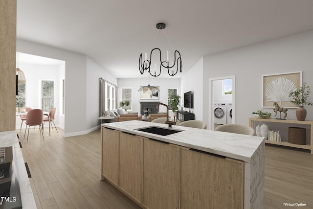 kitchen featuring sink, washer and dryer, a kitchen island with sink, pendant lighting, and light hardwood / wood-style floors