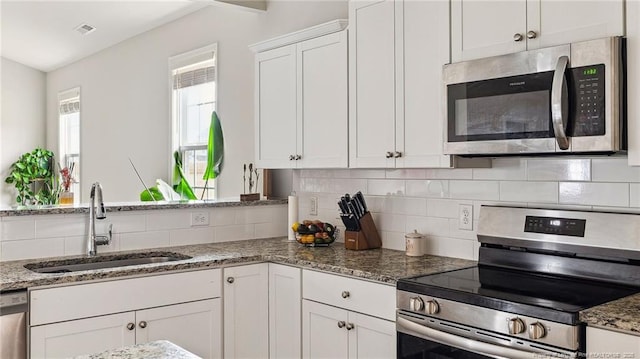 kitchen featuring white cabinets, stainless steel appliances, tasteful backsplash, dark stone countertops, and sink