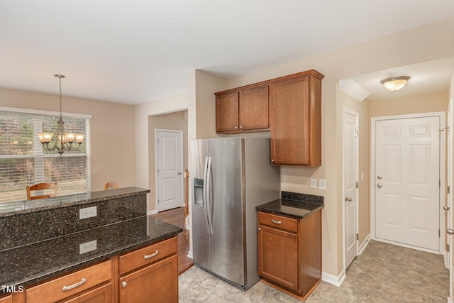 kitchen featuring dark stone counters, hanging light fixtures, brown cabinetry, and stainless steel fridge