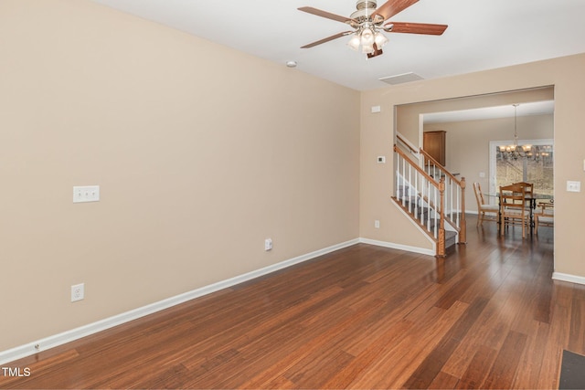 spare room featuring dark wood finished floors, stairway, baseboards, and ceiling fan with notable chandelier