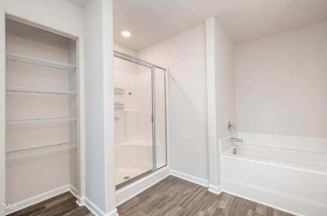 full bathroom featuring a stall shower, baseboards, wood finished floors, a garden tub, and a walk in closet