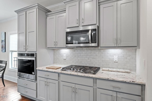 kitchen with stainless steel appliances, dark hardwood / wood-style flooring, backsplash, gray cabinets, and ornamental molding