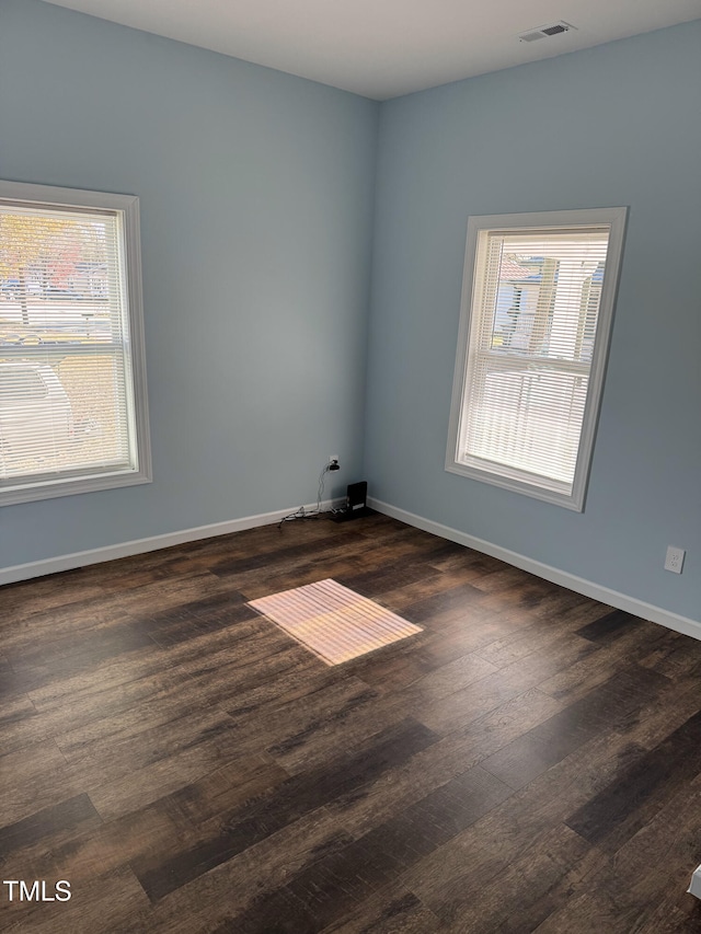 spare room featuring dark wood finished floors, visible vents, and baseboards