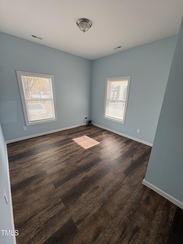 unfurnished room featuring dark wood-type flooring, a healthy amount of sunlight, and visible vents