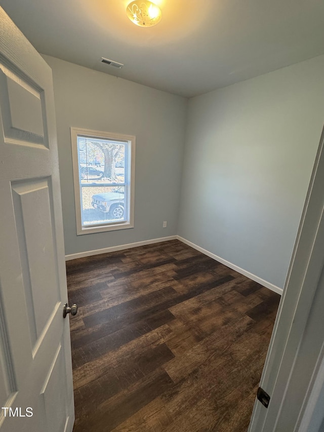 empty room with visible vents, dark wood finished floors, and baseboards