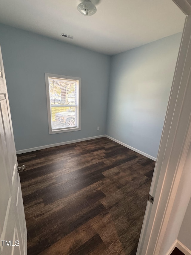 spare room with baseboards, visible vents, and dark wood finished floors