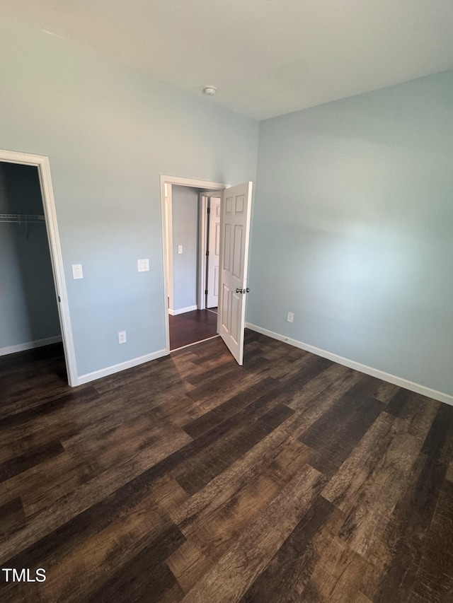 unfurnished bedroom featuring a closet, baseboards, a walk in closet, and dark wood-type flooring