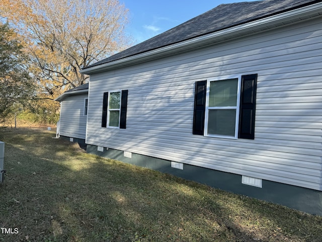 view of side of property featuring roof with shingles, crawl space, and a lawn