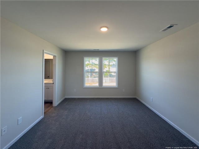 unfurnished bedroom with ensuite bath, baseboards, visible vents, and dark carpet