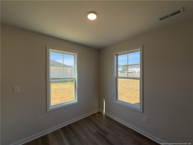 empty room featuring a water view, dark wood finished floors, visible vents, and baseboards