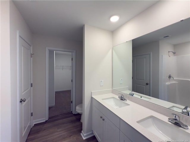 bathroom with double vanity, toilet, a walk in closet, and a sink